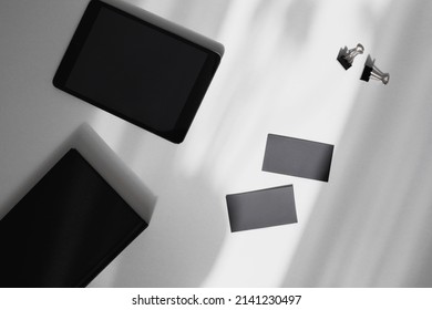 Male Home Office Desk With Black Note Pad, Digital Tablet, Blank Business Cards On Gray With Sunbeam.