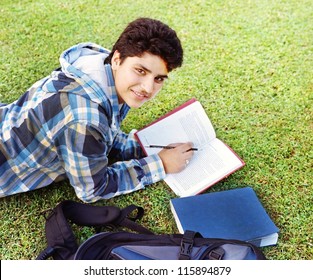 Male Indian / Asian College Student Lying / Studying Over The Grass.