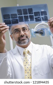 Male Indian Dentist Examining X-ray Report In Clinic