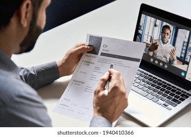 Male indian hr, recruiter or employer holding cv having online virtual job interview meeting with african candidate on video call. Distance remote recruitment conference chat. Over shoulder view. - Shutterstock ID 1940410366