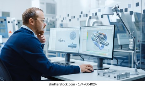 Male Industrial Engineer Solving Problems, Working on a Personal Computer, Two Monitor Screens Show CAD Software with 3D Prototype of Hybrid Electric Engine Being Tested. Working Modern Factory