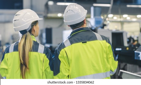 Male Industrial Worker and Female Chief Mechanical Engineer in Walk Through Manufacturing Plant while Discuss Factory's New Project. Facility Has Working Machinery. - Shutterstock ID 1335834062