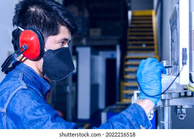 Male Industrial Worker With Protective Mask And Hearing Protectors Configures A Machine Using A Pencil And Touch Display