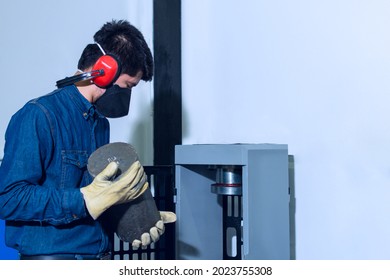 Male Industrial Worker With Protective Mask And Hearing Protectors Holding A Concrete Cylinder On Test Laboratory