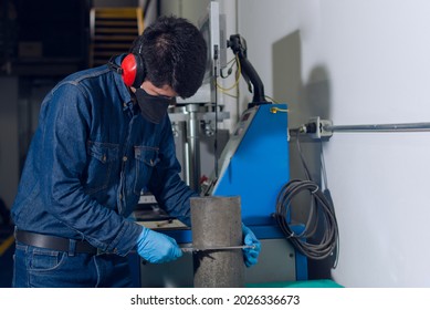 Male Industrial Worker With Protective Mask And Hearing Protectors Measuring A Concrete Cylinder