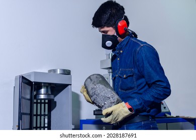 Male Industrial Worker With Protective Mask And Hearing Protectors Loading A Concrete Cylinder For Testing