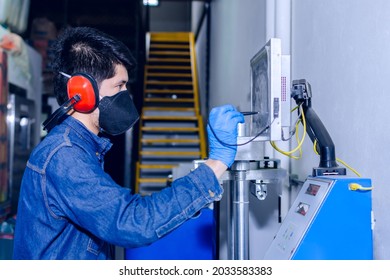 Male Industrial Worker With Protective Mask And Hearing Protectors Configures A Machine Using A Pencil And Touch Display