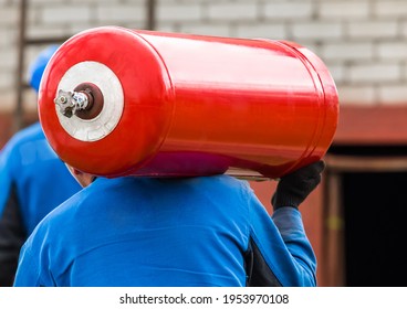 A Male Industrial Worker Walks With A Gas Cylinder To A Gas Car. Transportation And Installation Of A Propane Bottle To Residential Buildings.