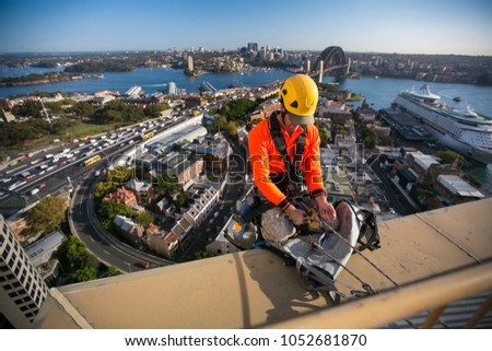 Male industry rope access using twin rope wearing helmet working and abseiling, off on construction building high rise site, back ground is Sydney harbour bridge in Sydney city CBD, Australia   