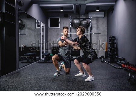 A male instructor assists women in a special suit for EMS technology while performing stability squats in a modern gym concept. Revolution in training, body rehabilitation