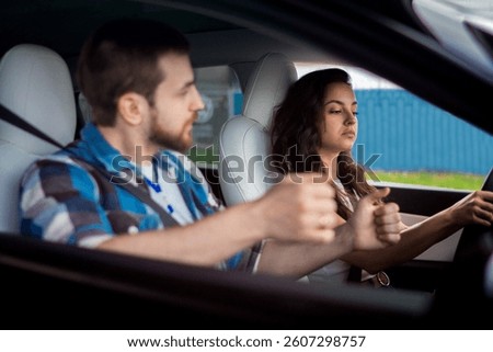 Male instructor controlling and checking during studying in school. Young woman driving and looking at the road. Driving test, driver courses, exam concept