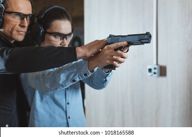 Male Instructor Helping Customer To Shoot With Gun In Shooting Range
