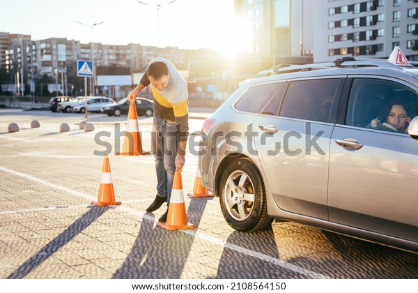 Male\
instructor teaching learner driver to park a car on the training\
ground with traffic cones at the driving\
school.