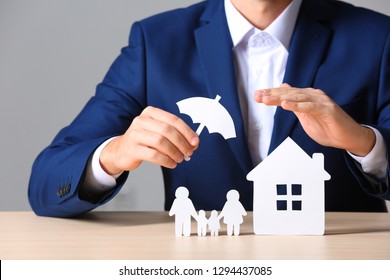 Male Insurance Agent Covering Paper Family And Home With Umbrella Cutout At Table, Closeup