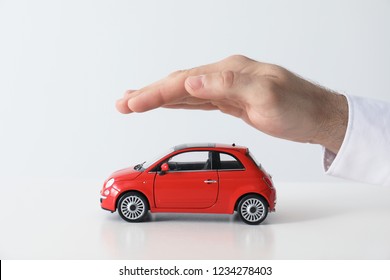 Male Insurance Agent Covering Toy Car On White Background, Closeup