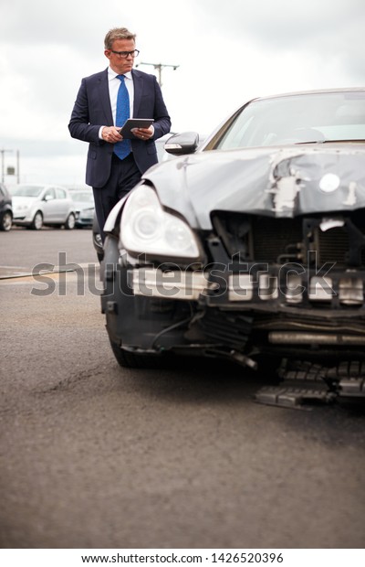 Male Insurance Loss Adjuster With\
Digital Tablet Inspecting Damage To Car From Motor\
Accident