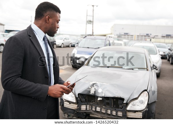 Male Insurance Loss Adjuster With\
Digital Tablet Inspecting Damage To Car From Motor\
Accident