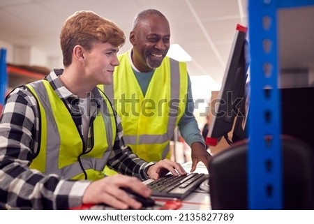 Male Intern With Supervisor Working In Busy Modern Warehouse On Computer Terminal Foto d'archivio © 