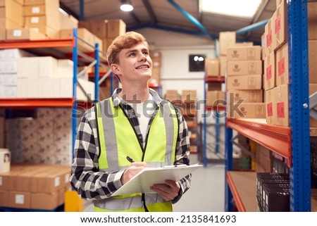 Male Intern Working Inside Warehouse Checking Stock On Shelves Using Clipboard Foto d'archivio © 