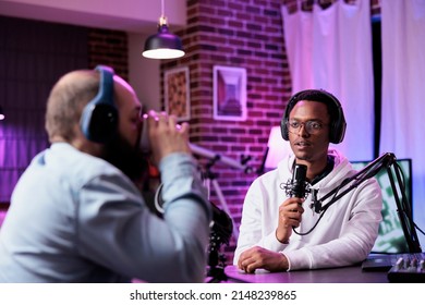 Male internet vlogger recording podcast chat with guest, using sound equipment at desk. Cheerful people live broadcasting discussion for social media web, streaming online content.