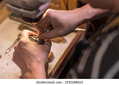 A male jeweler fixes precious stones on a silver pendant