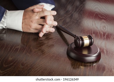 Male Judge Rests Folded Hands Behind Gavel with American Flag Reflection on Wooden Table. - Powered by Shutterstock