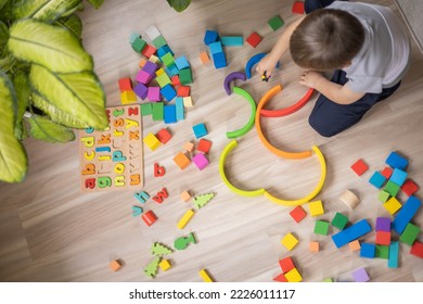 Male kid playing rainbow Montessori wooden natural material early development plaything sitting on floor at home. Cute baby child building labyrinth with colored curved arch ecology cubes blocks - Shutterstock ID 2226011117