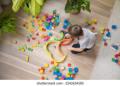 Male kid playing rainbow Montessori wooden natural material early development plaything sitting on floor at home. Cute baby child building labyrinth with colored curved arch ecology cubes blocks - Powered by Shutterstock