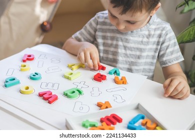 Male kid playing with wooden eco friendly alphabet letters board on table top view. Intellectual game preschool primary education early development font characters for learning reading and writing