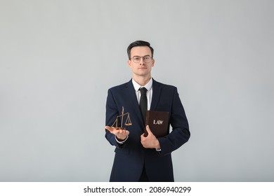 Male lawyer with scales of justice and book on grey background