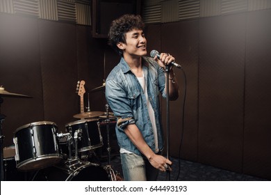 Male Lead Vocalist Singing In Studio With Music Instrument Background.