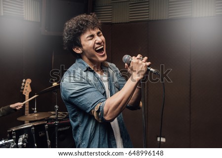 Male lead vocalist singing in studio with music instrument background.