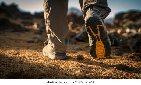 Male legs in trekking shoes close-up, a man walks along a trail among rocky mountains, hiking on a volcano, sand dunes at sunset. - Powered by Shutterstock