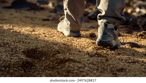 Male legs in trekking shoes close-up, a man walks along a trail among rocky mountains, hiking on a volcano, sand dunes at sunset. - Powered by Shutterstock