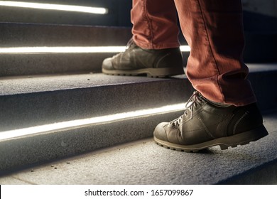 Male legs in walking boots climb the lit stone steps on a winter evening.