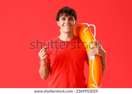 Male lifeguard with whistle and ring buoy on red background