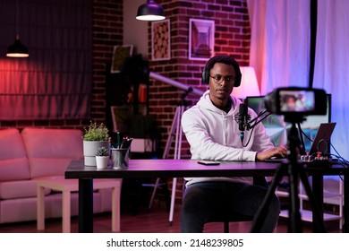 Male lifestyle vlogger recording live podcast vlog on camera, filming livestream in studio with neon lights. Social media influencer vlogging internet video as channel content.