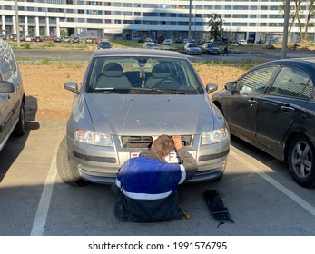 A Male Locksmith Worker Repairs A Car Lying Under It Under The Hood In A Parking Lot. DIY Car Repair.