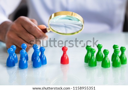 A Male Looking At Colorful Pawns With Magnifying Glass On The Reflective Desk