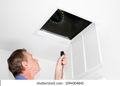 Male looking up into a ceiling air intake duct with a flashlight checking for maintenance. Person with a flashlight examining with a square opening of a home HVAC system