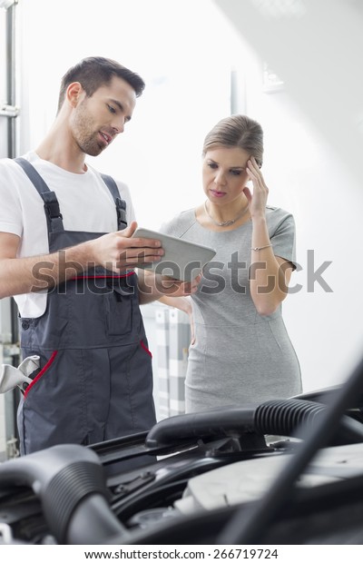Male maintenance engineer showing digital tablet\
to worried customer at\
workshop