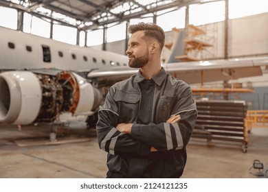 Male Maintenance Technician Keeping Arms Crossed And Looking Away While Standing In Aircraft Repair Station