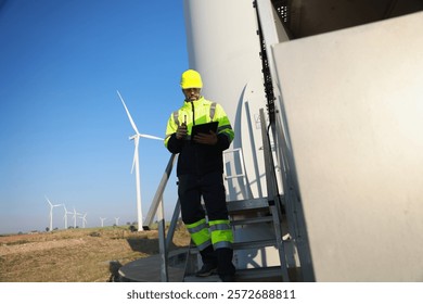 A male maintenance technician in uniform uses a talkie and a digital tablet to work on a station wind turbine. Carbon neutrality and clean energy.