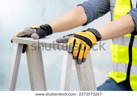 Male maintenance worker hands with protective yellow gloves holding aluminum step ladder at construction site. Building service tool and equipment
