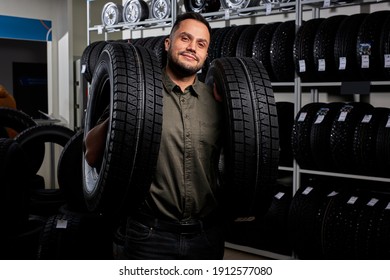 Male Making Purchase In Car Accessories Store, Pleasant And Satisfied Client In Casual Wear Stands Holding Car Tires. Portrait