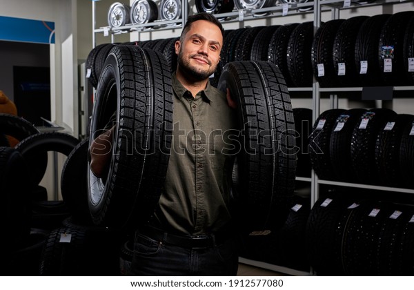 male making purchase in car accessories store,\
pleasant and satisfied client in casual wear stands holding car\
tires. portrait