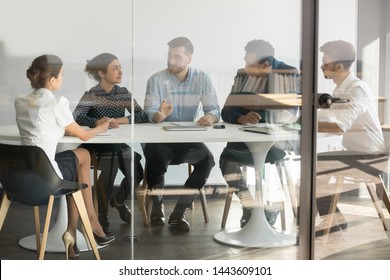 Male manager boss talking at group office meeting sit at conference table behind glass door, business team people listen to coach mentor leader teach interns consult clients at corporate briefing - Powered by Shutterstock