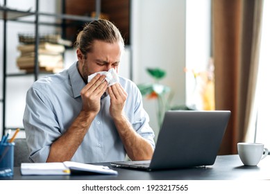 Male Manager Or Freelancer Sit At The Desk At Home Office, Working Distantly, Using Paper Tissue, Sneezing. Caucasian Unhealthy Man Feeling Unwell, Sick With Running Nose, Need A Rest