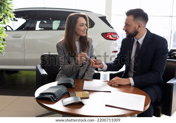 male manager selling a new car to a young\
woman in a car dealership, car rental\
concept