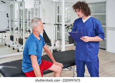 Male Manual Therapist Telling Prescriptions To His Male Patient At Rehabilitation Centre